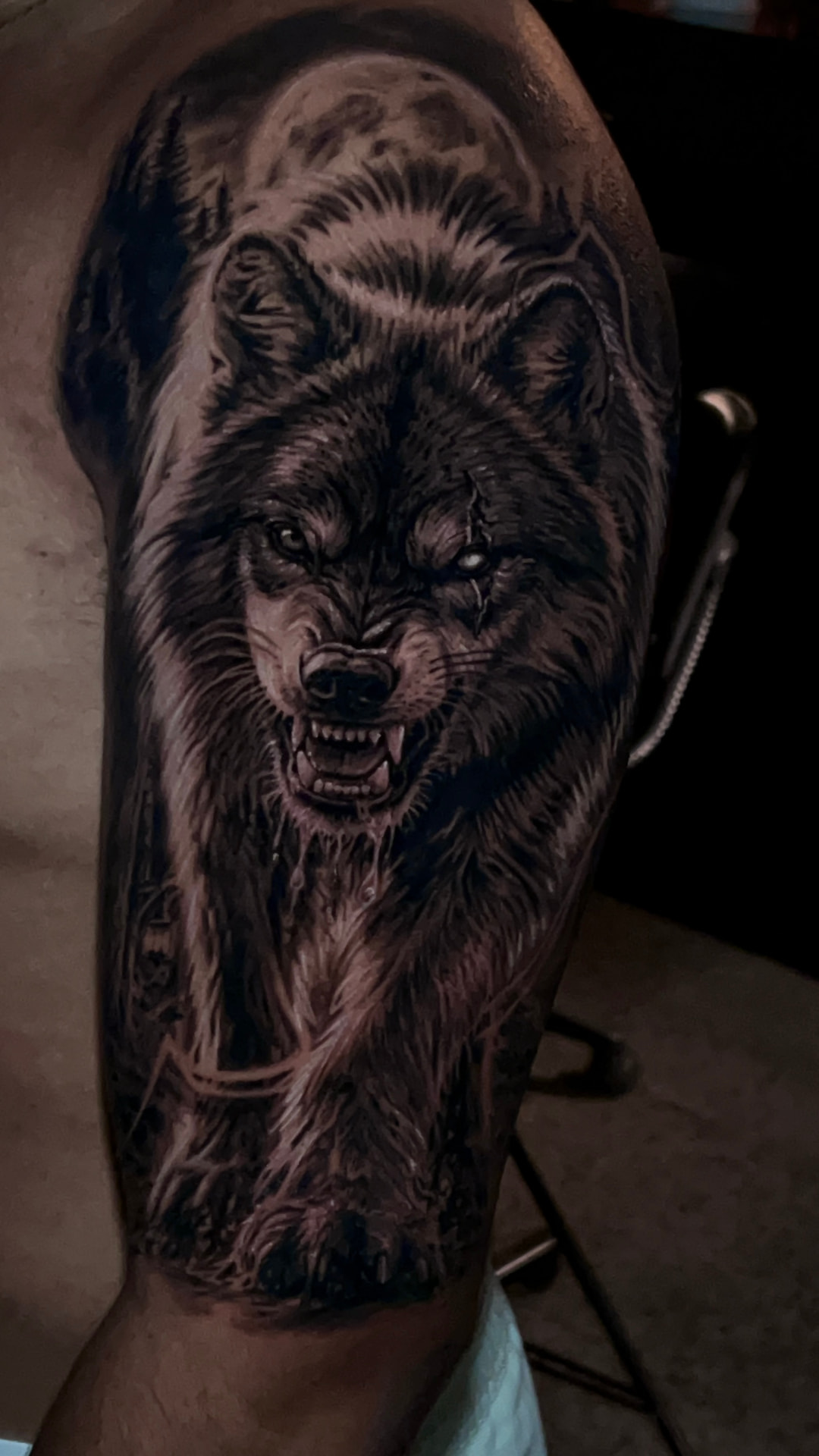 Tatuagem realista de lobo com lua e floresta no braço